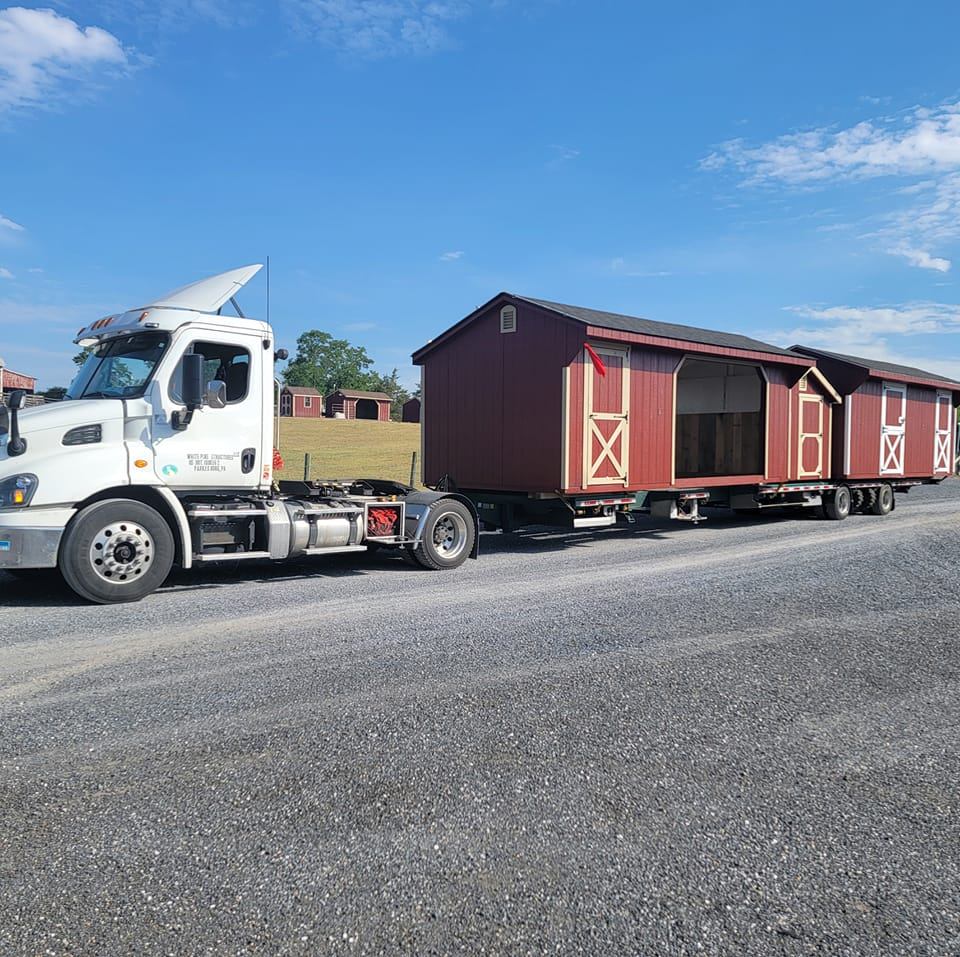 Wooden shed structure loaded on a specialized flatbed trailer during professional delivery transport