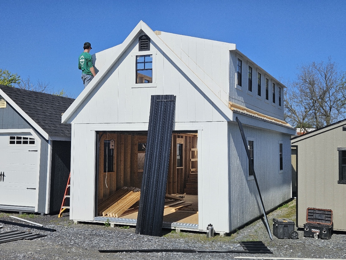 Rear view of a craftsman climbing the side of a two-story board-and-batten building under construction