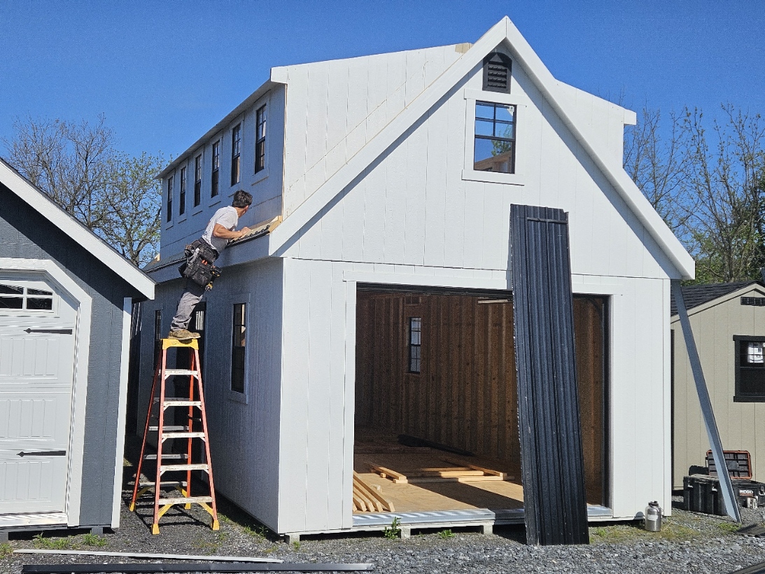 Amish craftsman on a ladder working on the front of a two-story white structure