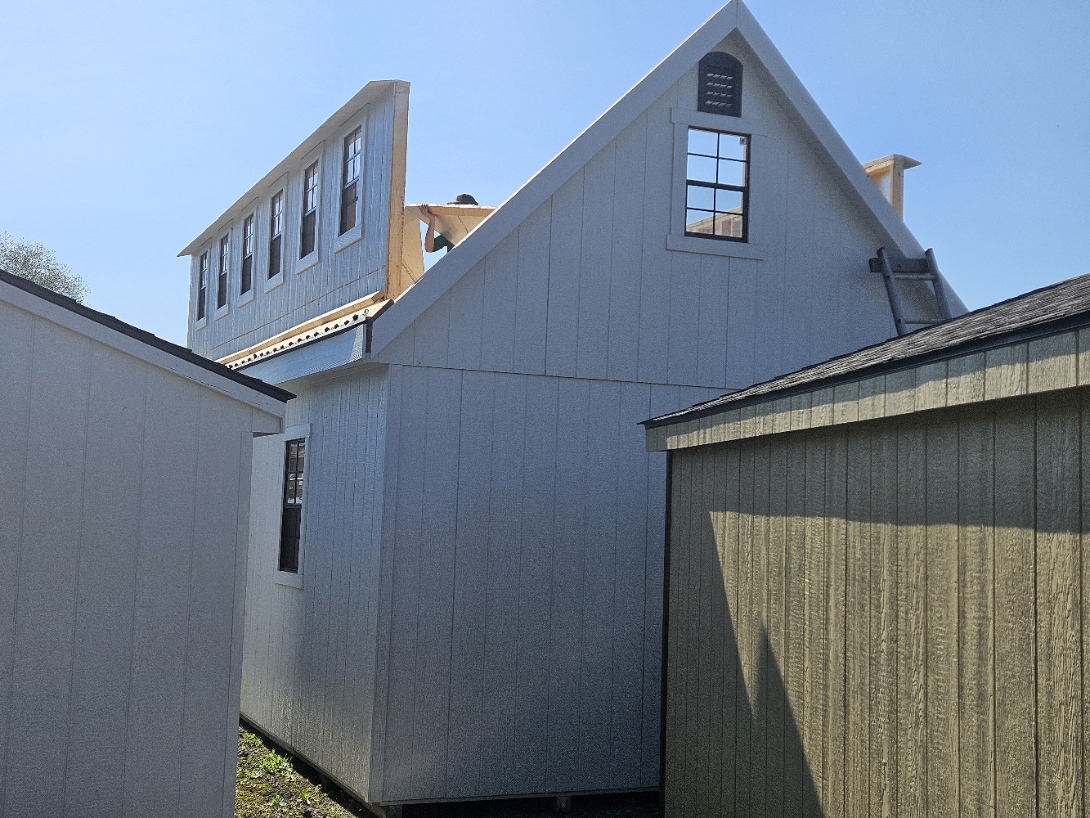 Close-up of a two-story dormer under construction — gray siding with exposed framing detail