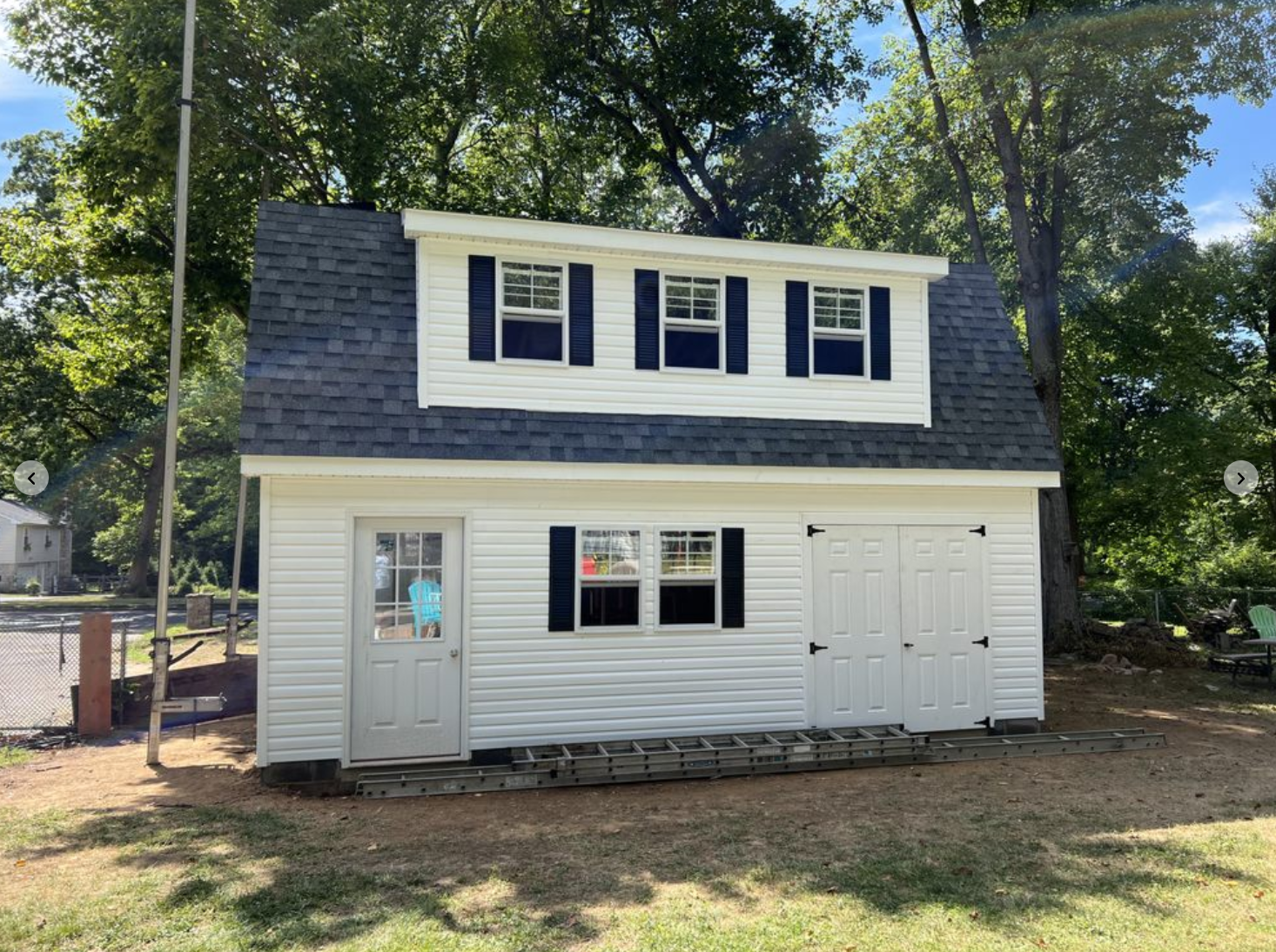 Completed two-story barn with white vinyl siding, navy blue shutters, and architectural shingle roof