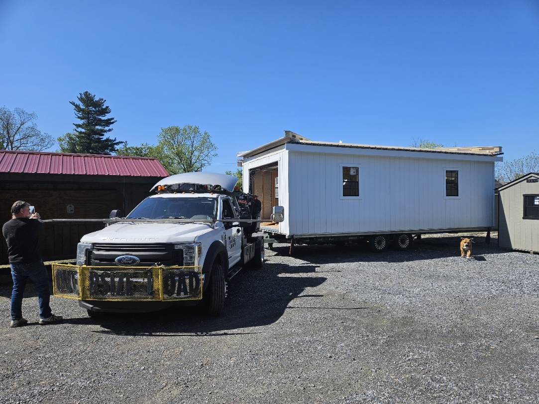 Ford F-550 hauling a two-story structure from the Parkesburg lot — roof framing exposed for highway clearance, ready for on-site completion
