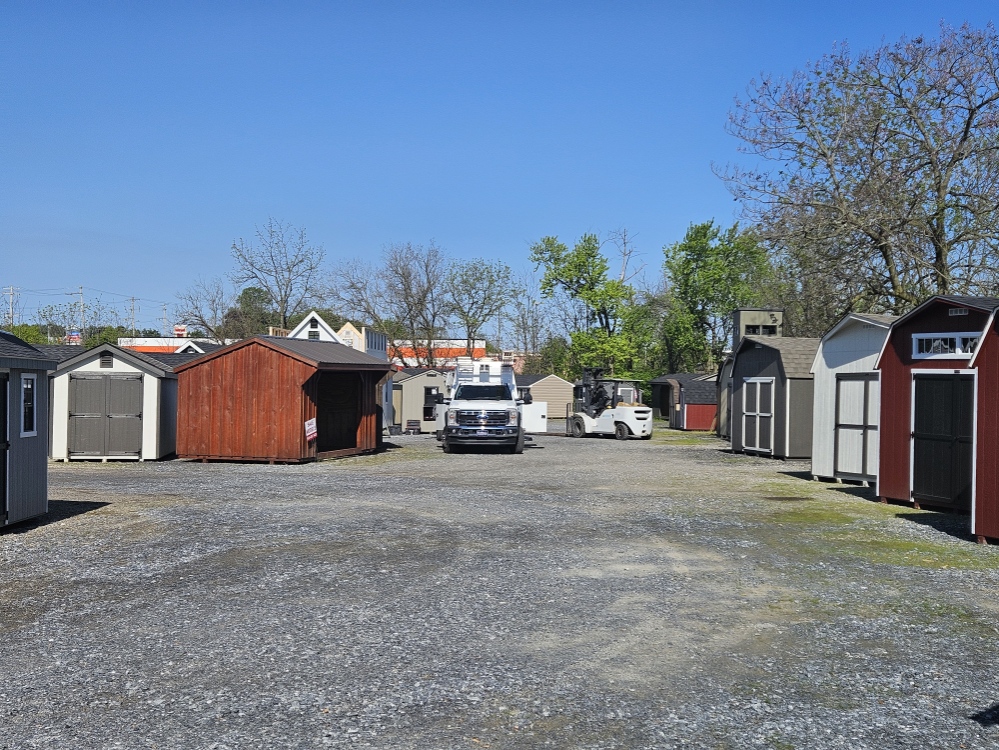 Panoramic view of the White Pine Structures Parkesburg lot — finished sheds, garages, and a delivery truck staged under a clear sky